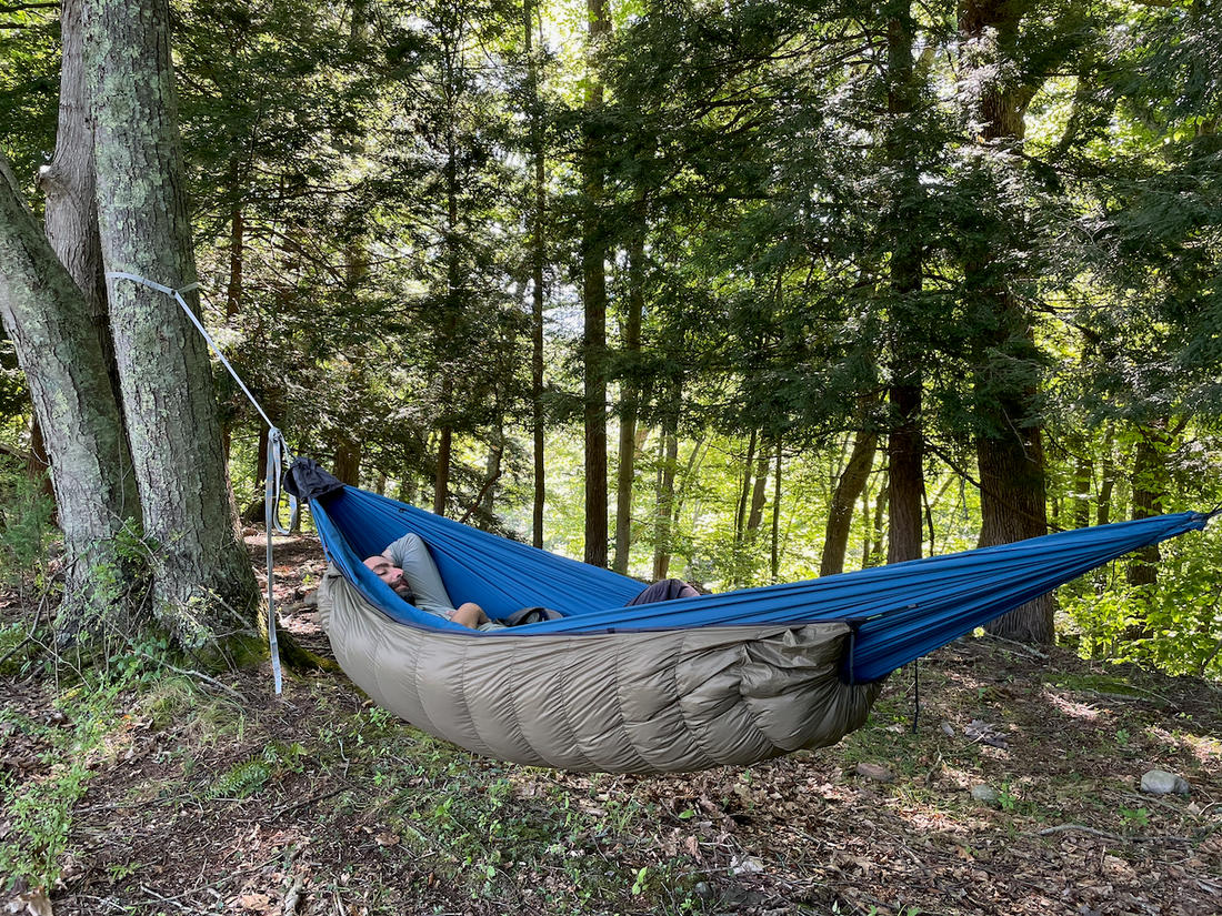 Camper resting in a hammock with a Jacks R Better down underquilt slung below in a summer forest