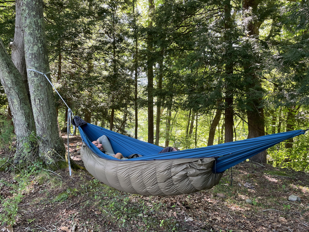 Camper resting in a hammock with a Jacks R Better down underquilt slung below in a summer forest